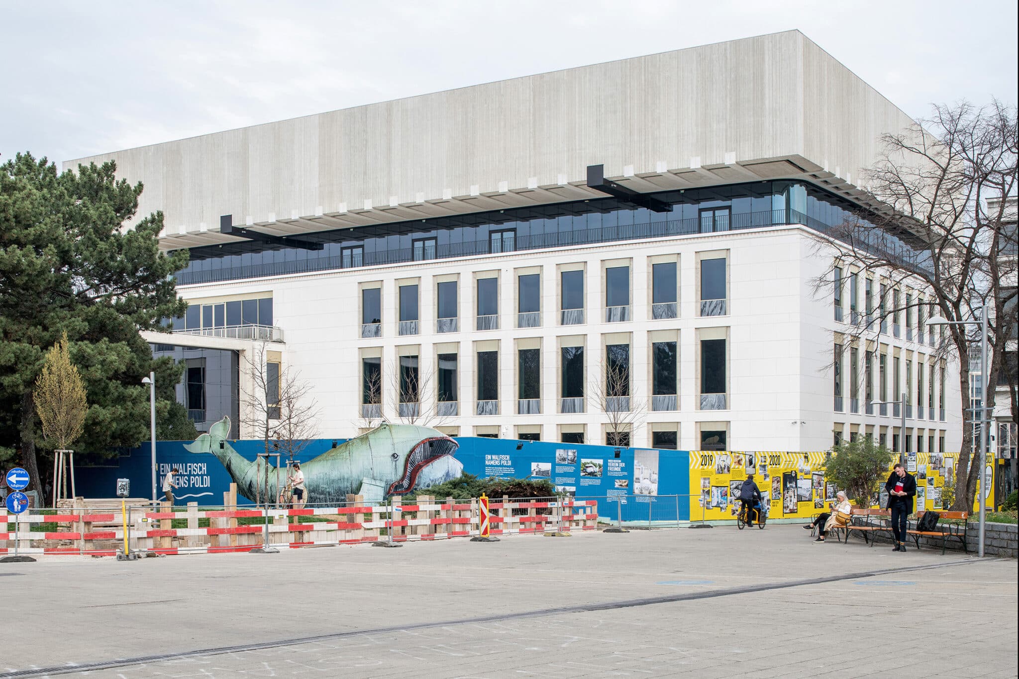 Wien Museum Neu © Kollektiv Fischka. Das Foto zeigt die neue Fassade des umgebauten Wien Museums. Der Baustellenzaun ist dabei mit Streetart Elementen verziert. Auf dem Zaun ist eine Meereslandschaft mit einem Wal zu sehen.