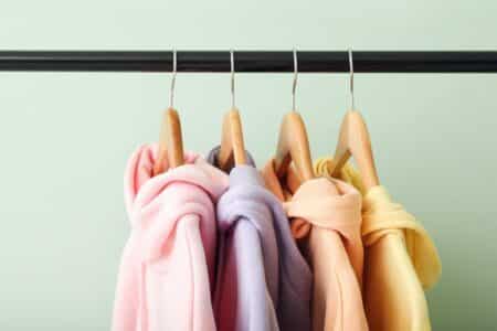 Rack with trendy hoodies near green wall, closeup