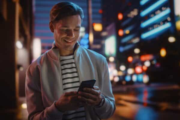 Portrait,Of,Man,Using,Smartphone,Walking,Through,Night,City,Street
