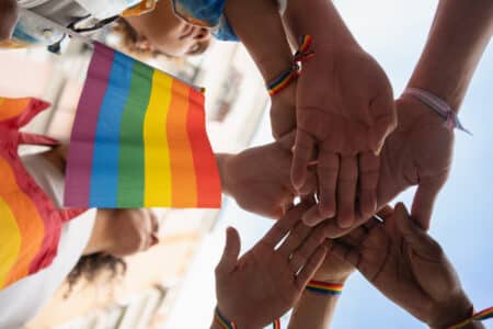 hands joined together holding pride flag outdoors utc