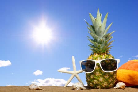 pineapple with sunglasses in sand against a sunny utc